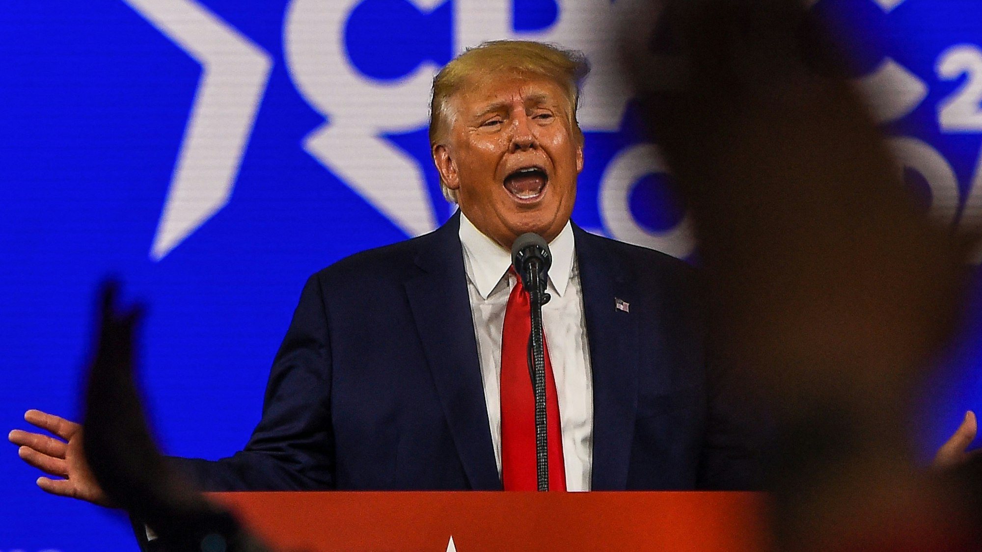 Donal Trump spricht mit ausgebreiteten Armen an einem Rednerpult in Florida.