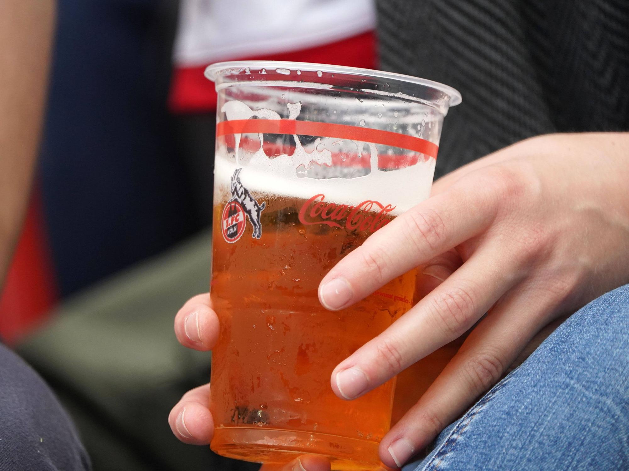 Ein FC-Fan hält einen Bierbecher in der Hand.