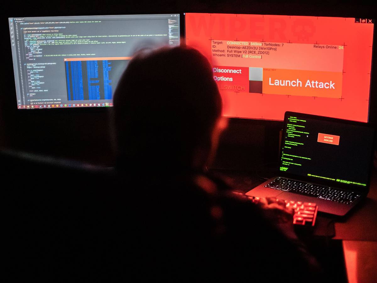 Das Symbolfoto vom 25.02.2022 aus Bad Oeynhausen (NRW) zeigt einen Mann vor Bildschirmen, die Hacker-Programme und eine fiktive Fernlösch-Software zeigen.