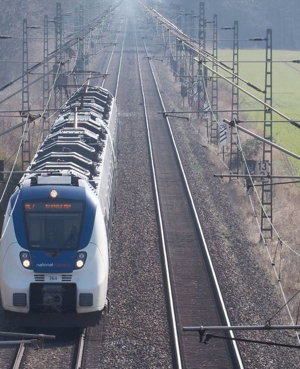 Eine Bahn steht auf den Gleisen, rechts und links Grünflächen und Gebüsch.