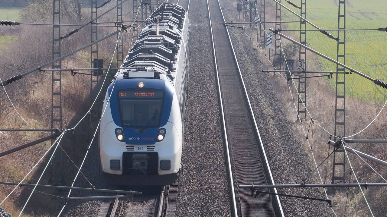 Eine Bahn steht auf den Gleisen, rechts und links Grünflächen und Gebüsch.