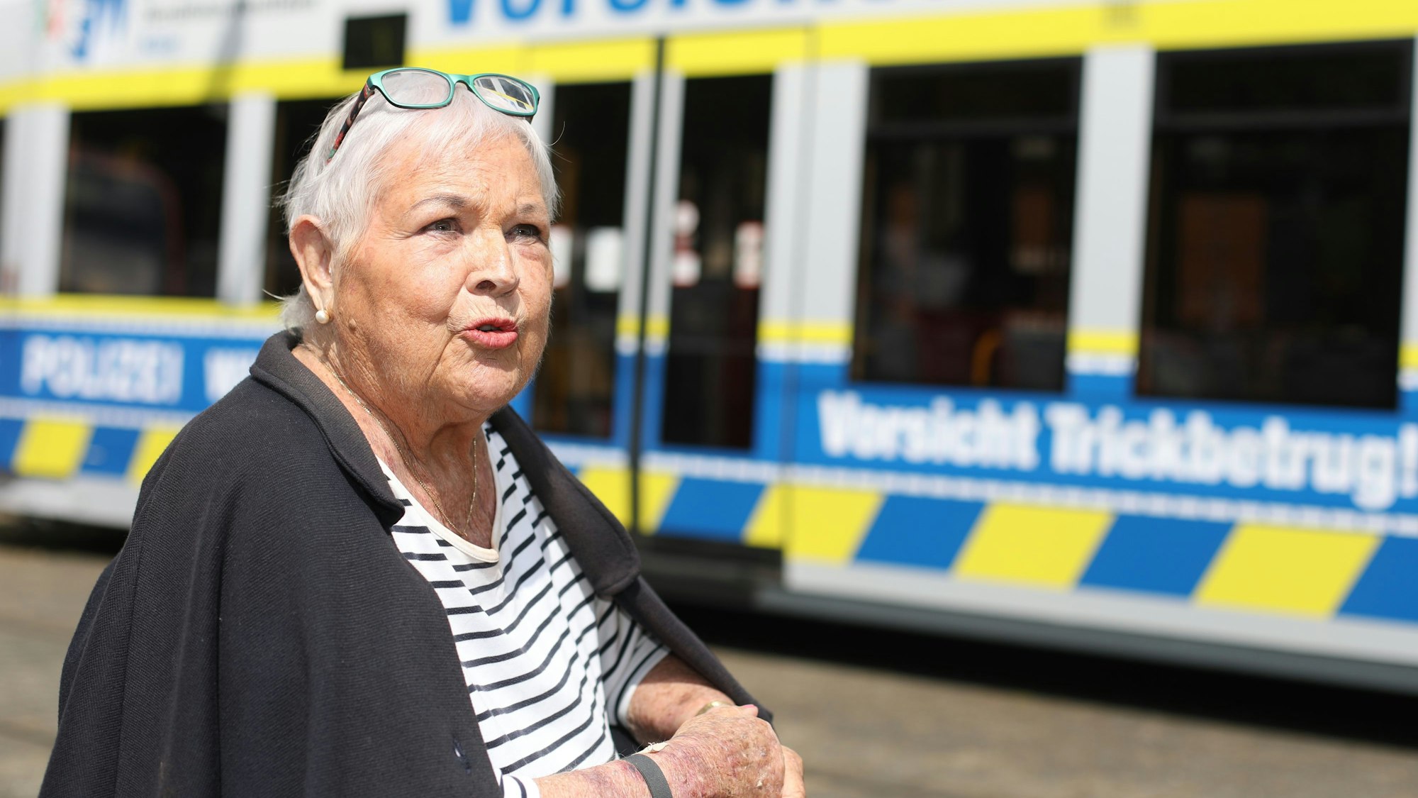 Ältere Frau sitzt vor einer Bahn der KVB.