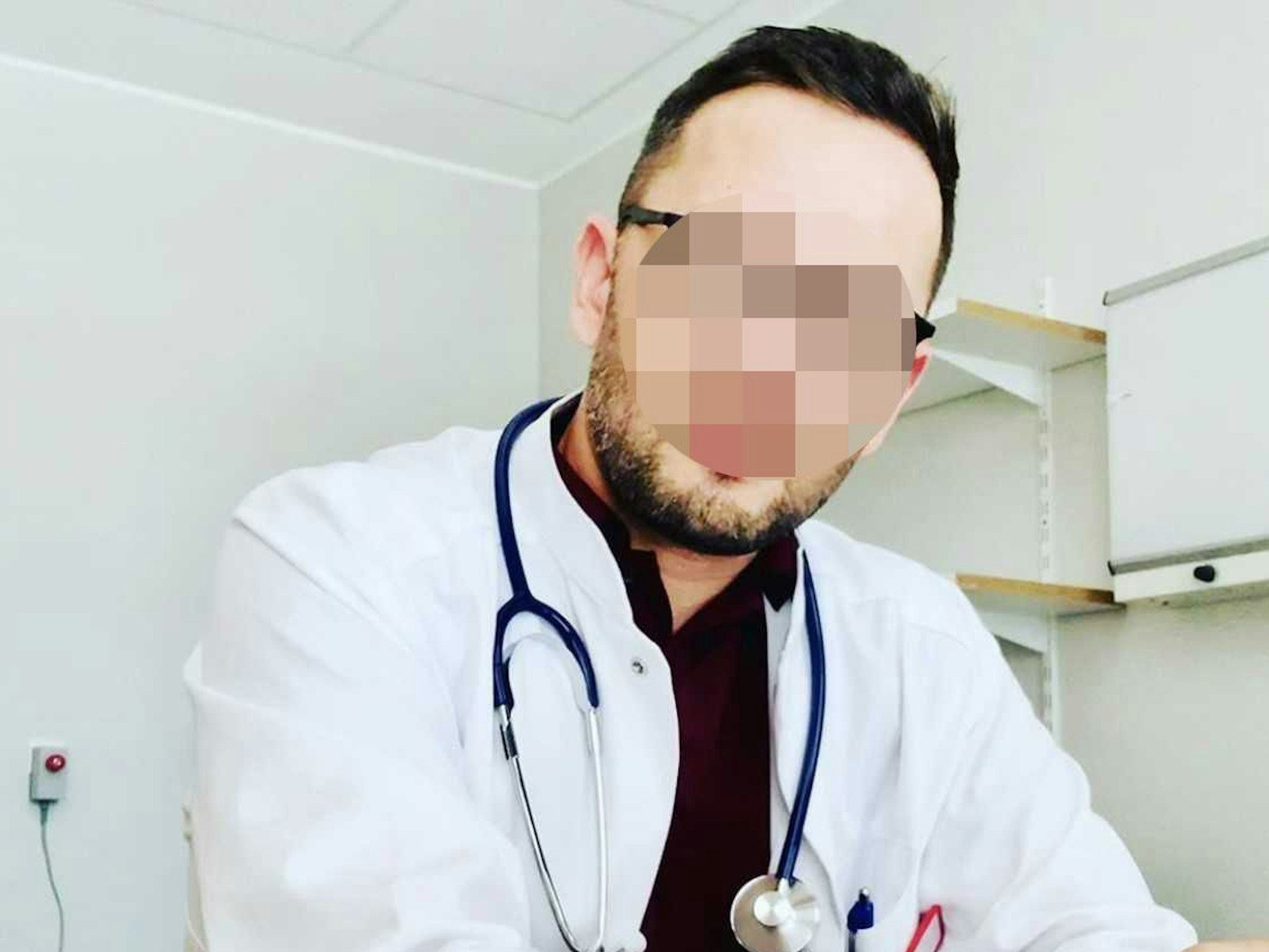 Ein Mann in einem Arztkittel sitzt an einem Tisch.