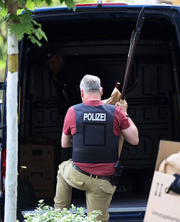Polizisten tragen Gegenstände, darunter mehrere Stichwaffen und Speere, aus dem Wohnhaus des Verdächtigen.