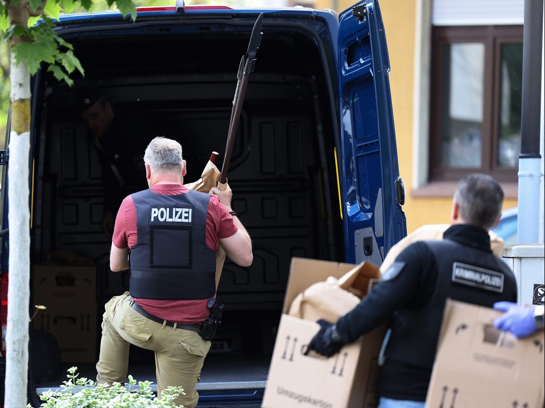 Polizisten tragen Gegenstände, darunter mehrere Stichwaffen und Speere, aus dem Wohnhaus des Verdächtigen.