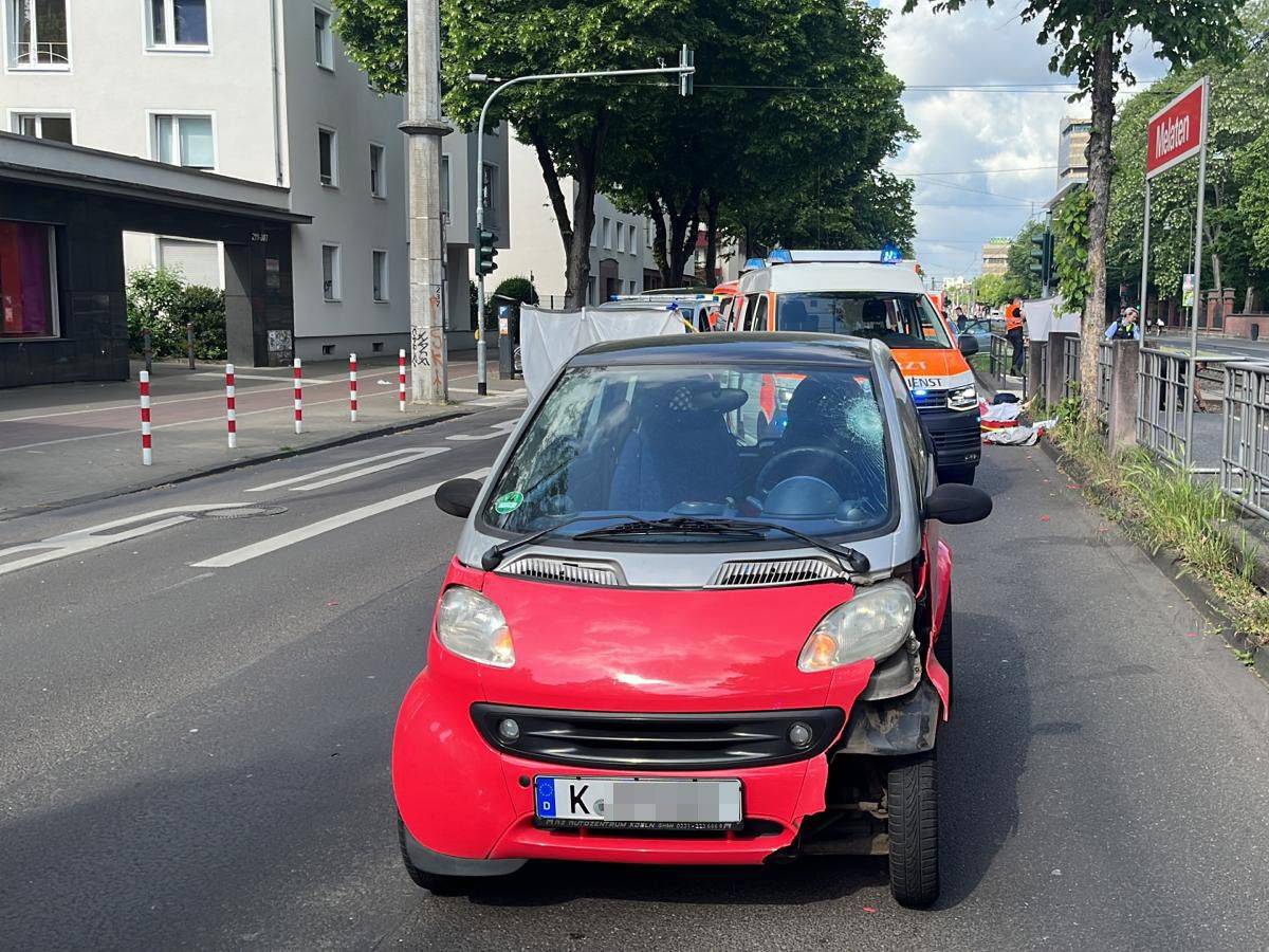 Ein Smart steht mit Beschädigungen auf der Straße, dahinter ein Rettungsfahrzeug.