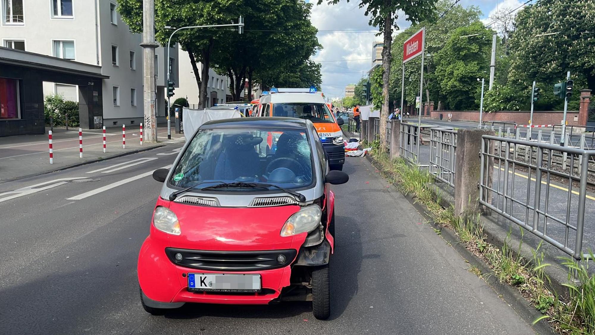 Ein Smart steht mit Beschädigungen auf der Straße, dahinter ein Rettungsfahrzeug.