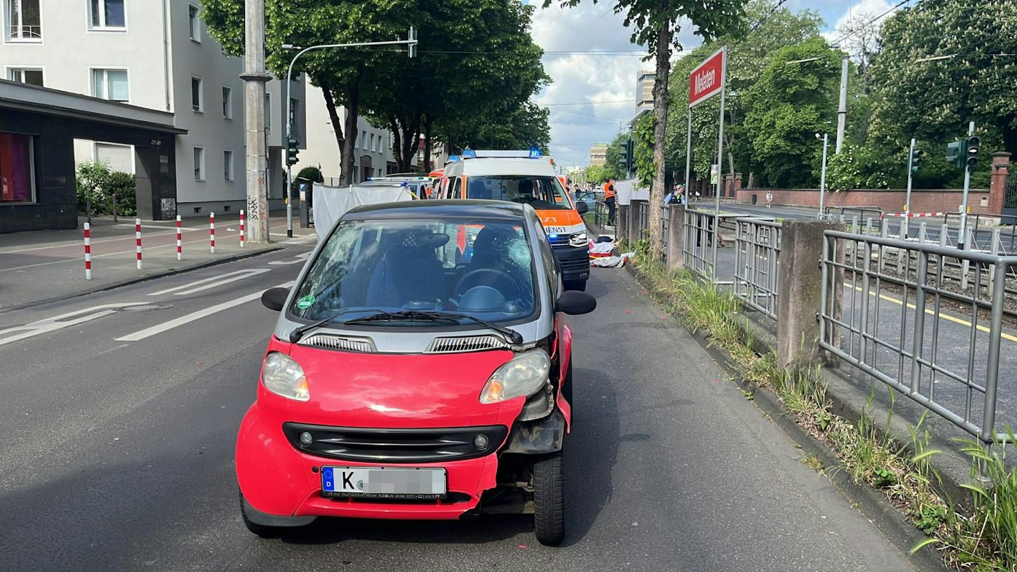 Ein Smart steht mit Beschädigungen auf der Straße, dahinter ein Rettungsfahrzeug.