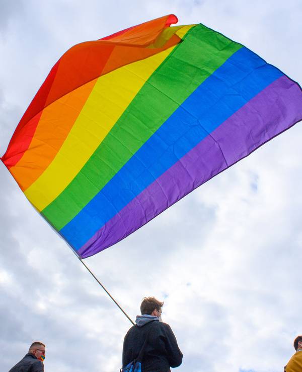 Teilnehmerinnen und Teilnehmer der Kundgebung des Bündnisses „#unteilbar Sachsen-Anhalt“ stehen mit einer wehenden Regenbogenfahne auf dem Domplatz.