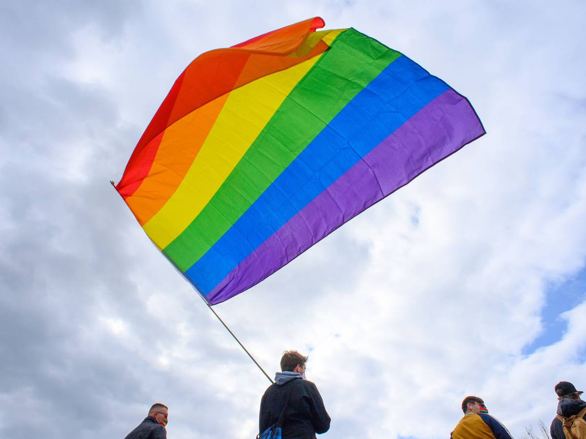 Teilnehmerinnen und Teilnehmer der Kundgebung des Bündnisses „#unteilbar Sachsen-Anhalt“ stehen mit einer wehenden Regenbogenfahne auf dem Domplatz.