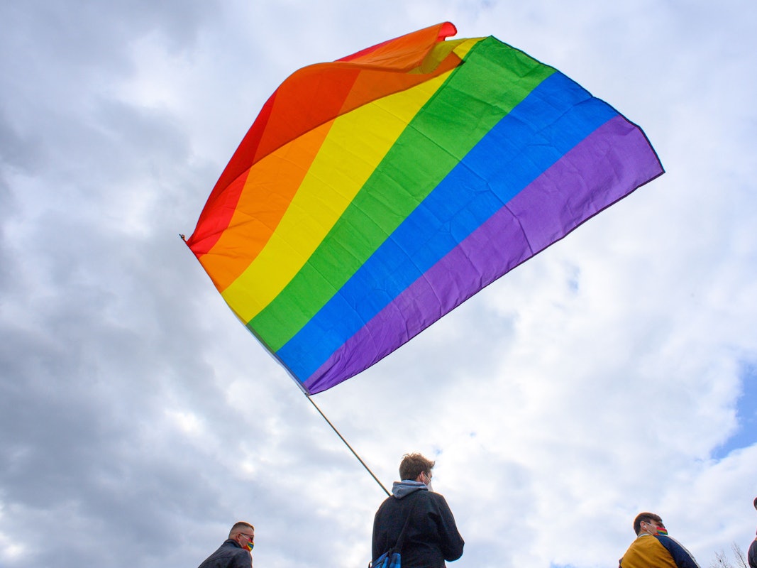 Teilnehmerinnen und Teilnehmer der Kundgebung des Bündnisses „#unteilbar Sachsen-Anhalt“ stehen mit einer wehenden Regenbogenfahne auf dem Domplatz.