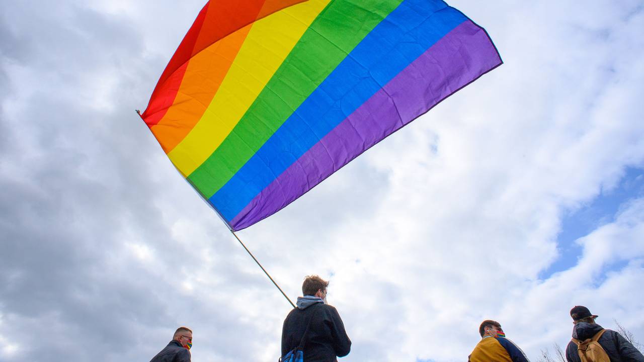 Teilnehmerinnen und Teilnehmer der Kundgebung des Bündnisses „#unteilbar Sachsen-Anhalt“ stehen mit einer wehenden Regenbogenfahne auf dem Domplatz.