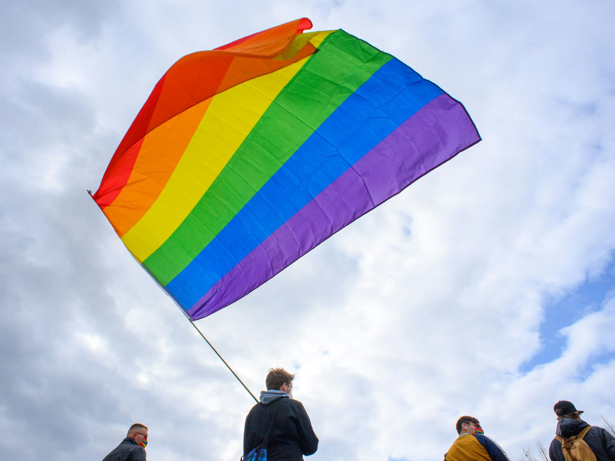 Teilnehmerinnen und Teilnehmer der Kundgebung des Bündnisses „#unteilbar Sachsen-Anhalt“ stehen mit einer wehenden Regenbogenfahne auf dem Domplatz.