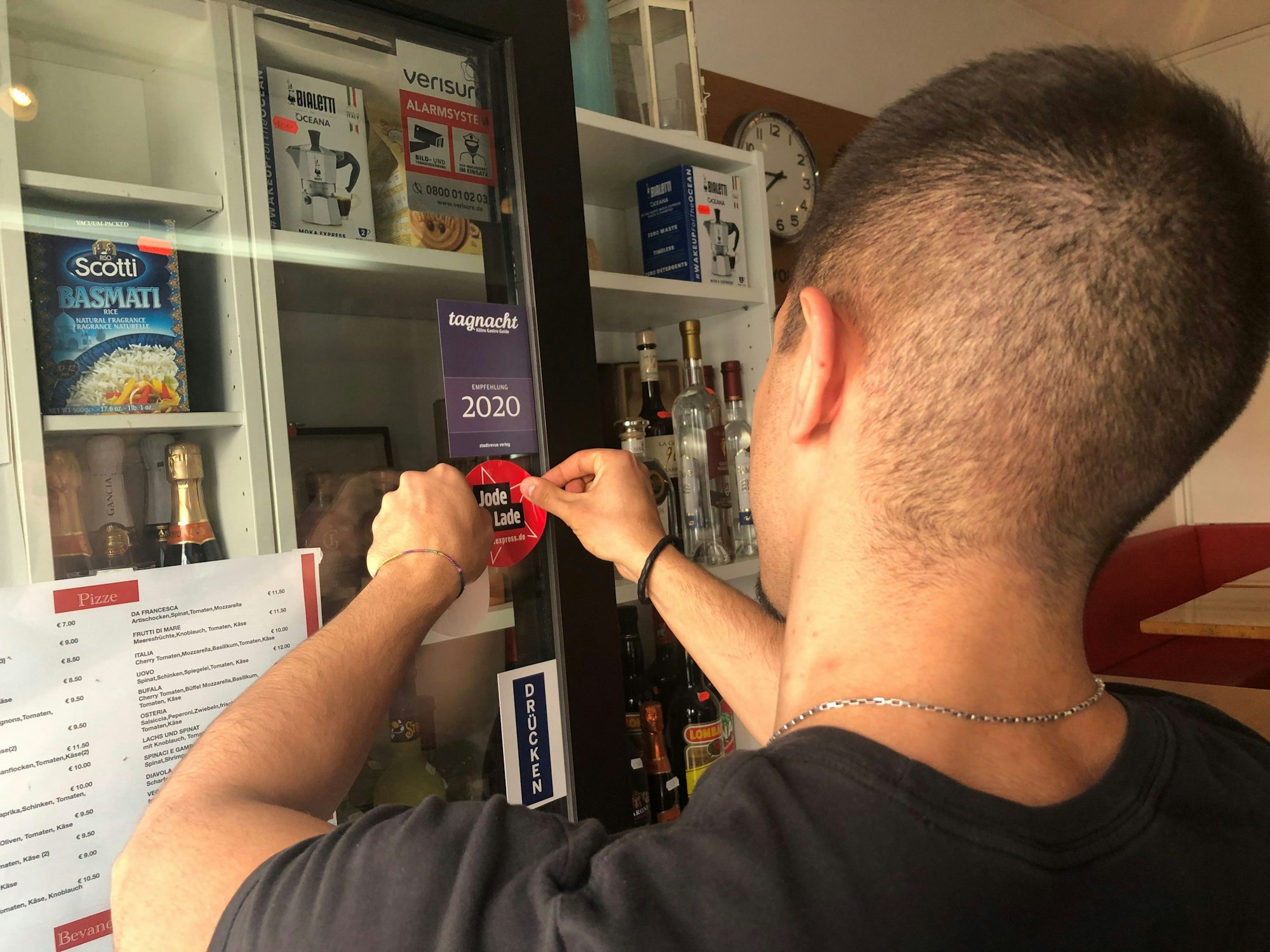 Domenico bringt den Jode Lade-Aufkleber an die Eingangstür der Osteria da Francesca an.