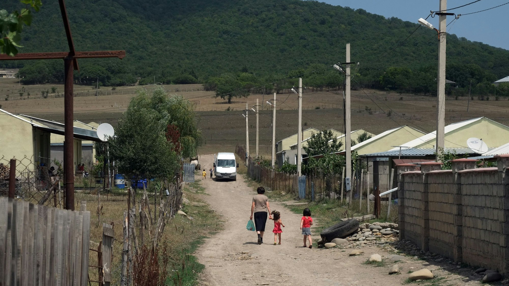 Eine Frau spaziert am 28.07.2018 mit ihren Kindern durch die staubigen Straßen des georgischen Flüchtlingsdorfes Freseti an der Grenze zu Südossetien. Die Separatistenregion will über den Beitritt zur russischen Föderation abstimmen lassen.