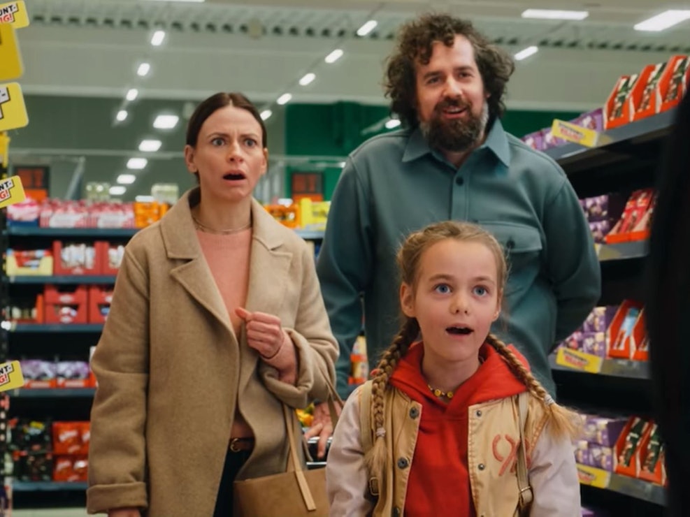 Eine Frau, ein Mann und ein Kind stehen mit aufgerissenem Mund in einem Supermarkt-Gang.