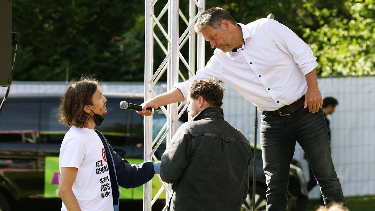 Robert Habeck (r, Bündnis 90/Die Grünen), Bundesminister für Wirtschaft und Klimaschutz, redet mit einen Demonstranten (l), der sich an die Bühne geklebt hat.