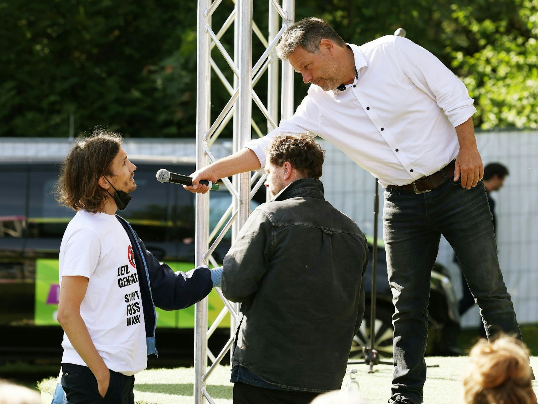 Robert Habeck (r, Bündnis 90/Die Grünen), Bundesminister für Wirtschaft und Klimaschutz, redet mit einen Demonstranten (l), der sich an die Bühne geklebt hat.