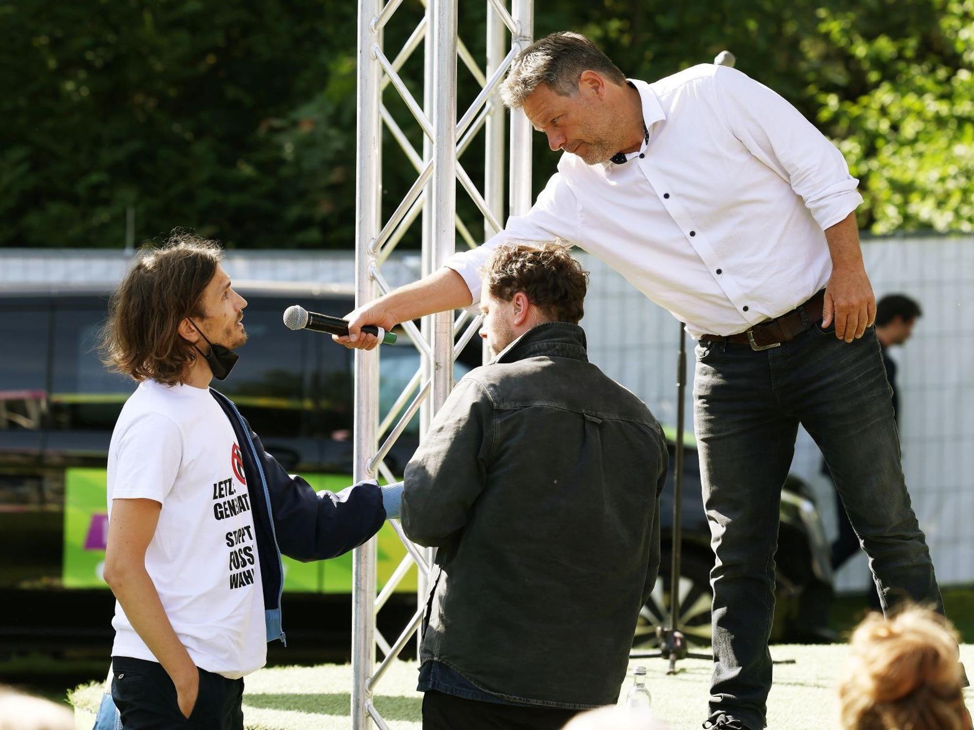 Robert Habeck (r, Bündnis 90/Die Grünen), Bundesminister für Wirtschaft und Klimaschutz, redet mit einen Demonstranten (l), der sich an die Bühne geklebt hat.