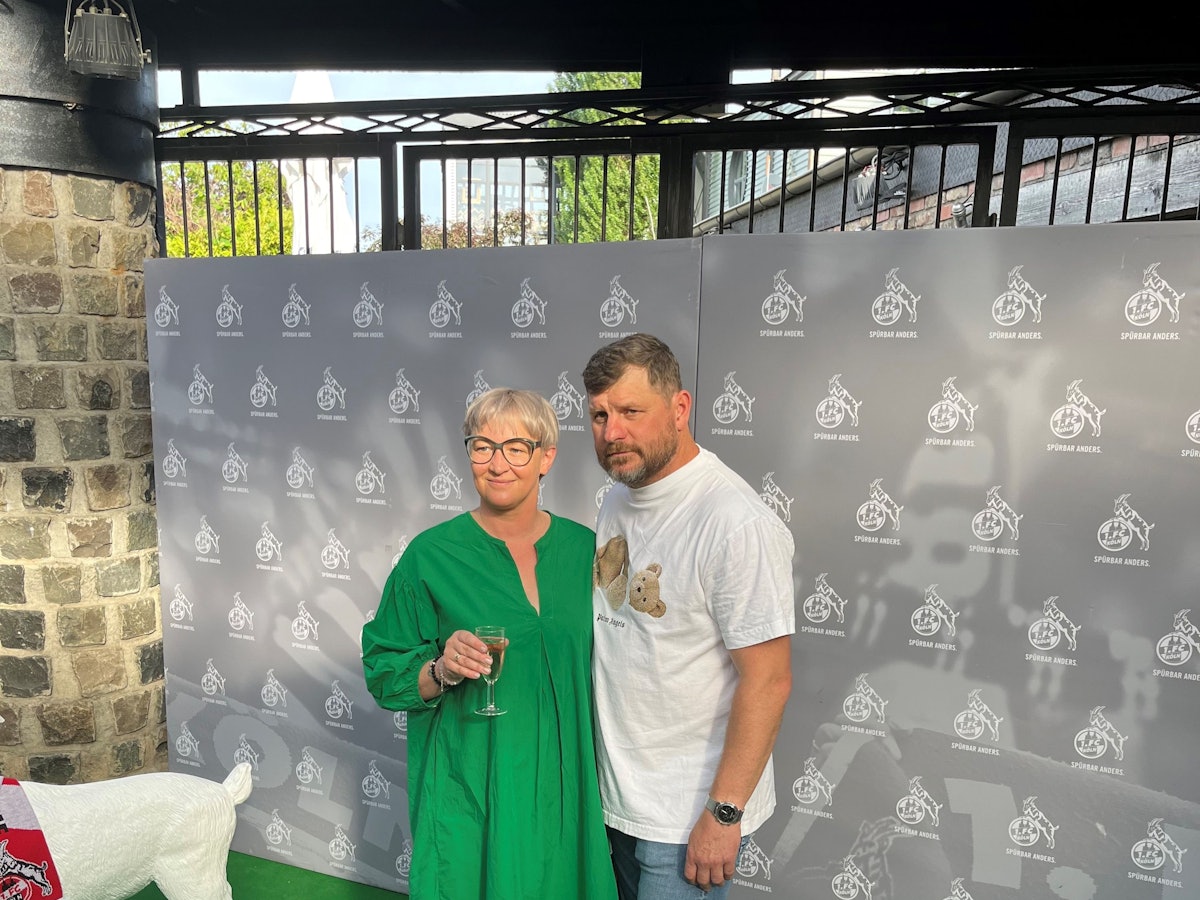 Steffen Baumgart und seine Frau Katja werden vor einem FC-Hintergrund beim Saison-Ausklang abgelichtet.