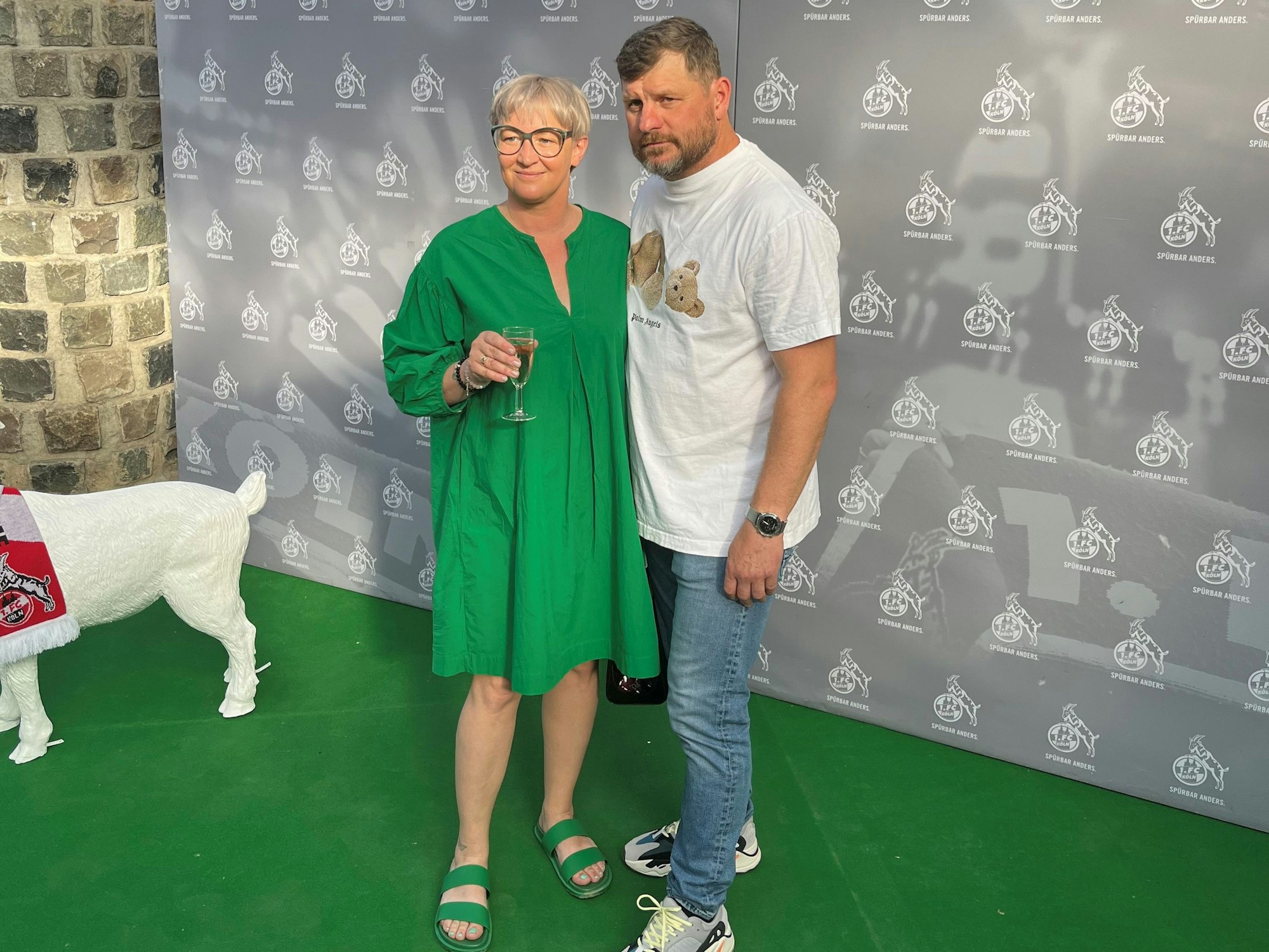 Steffen Baumgart und seine Frau Katja werden vor einem FC-Hintergrund beim Saison-Ausklang abgelichtet.
