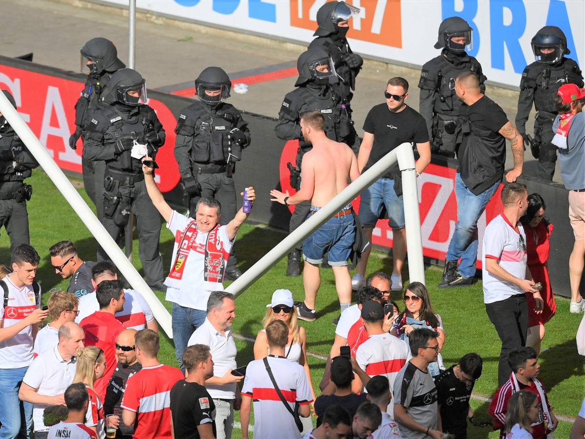 Zahlreiche Fans stehen nach dem Platzsturm vor dem inzwischen gebrochenen Tor auf dem Rasen des VfB Stuttgart. Im Hintergrund zahlreiche Polizeikräfte.