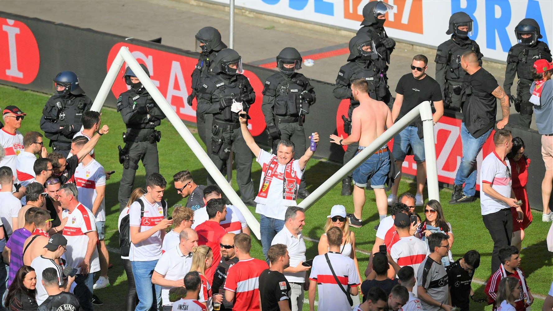 Zahlreiche Fans stehen nach dem Platzsturm vor dem inzwischen gebrochenen Tor auf dem Rasen des VfB Stuttgart. Im Hintergrund zahlreiche Polizeikräfte.