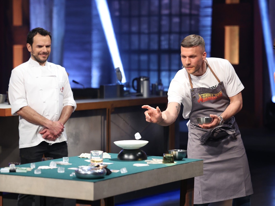 Lucas Podolski (r.) versucht, Eiswürfel in ein Whiskey-Glas zu werfen. Daneben steht Steffen Henssler (l.) in der Vox-Show „Grill den Henssler“ am 15. Mai 2022.
RTL/Frank Hempel
