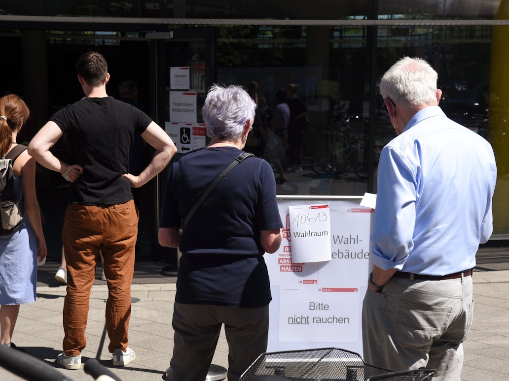 Menschen stehen vor einem Wahllokal in Köln in einer Schlange.