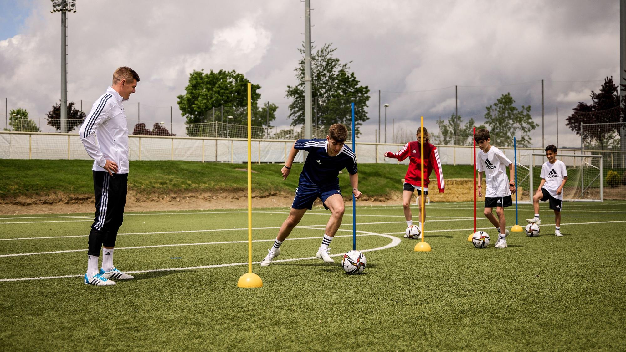 Toni Kroos beobachtet Kinder, die um Stangen dribbeln.