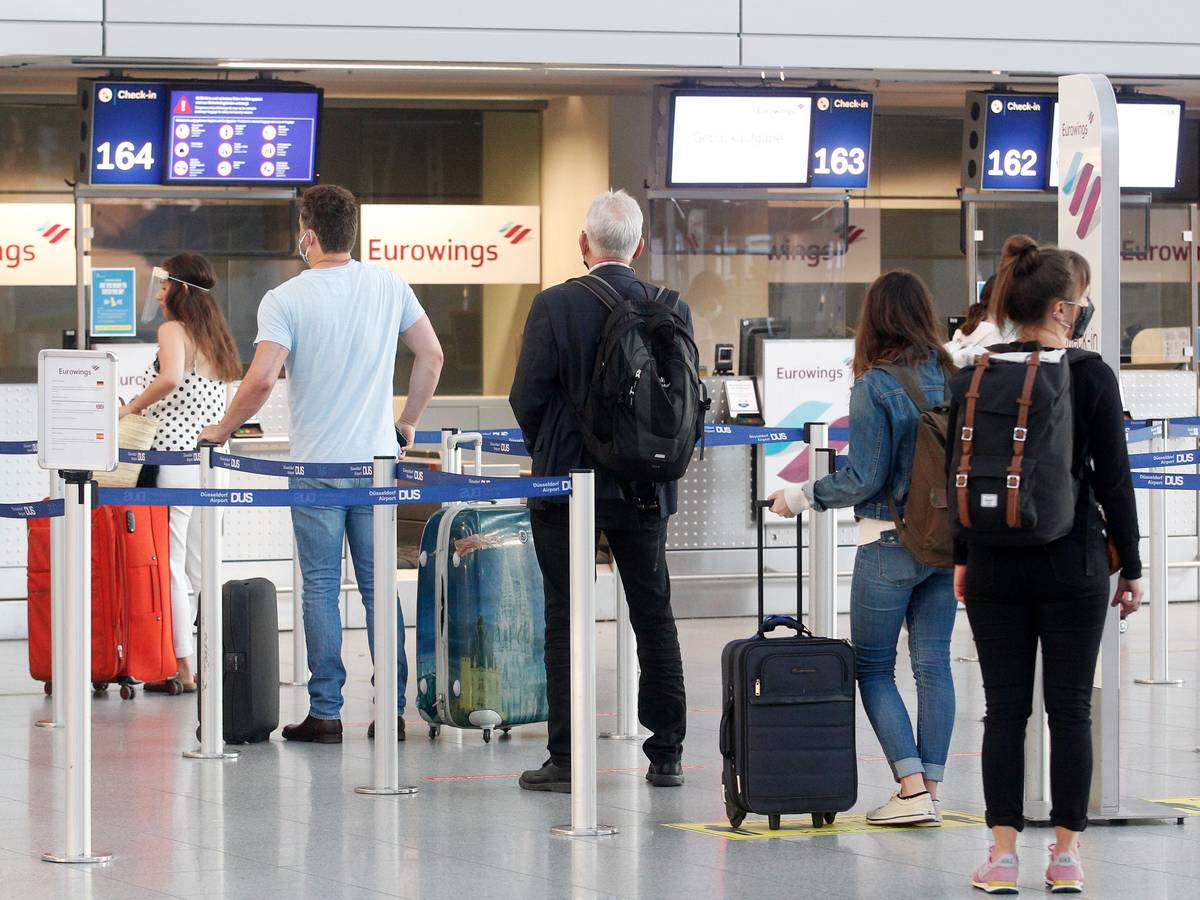 Fluggäste mit Masken warten am Düsseldorfer Flughafen vor einem Check-In-Schalter auf ihre Abfertigung.