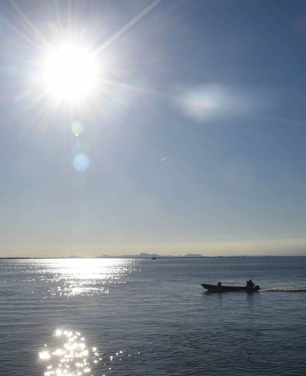 Ein Boot fährt bei Sonnenschein über einen See.