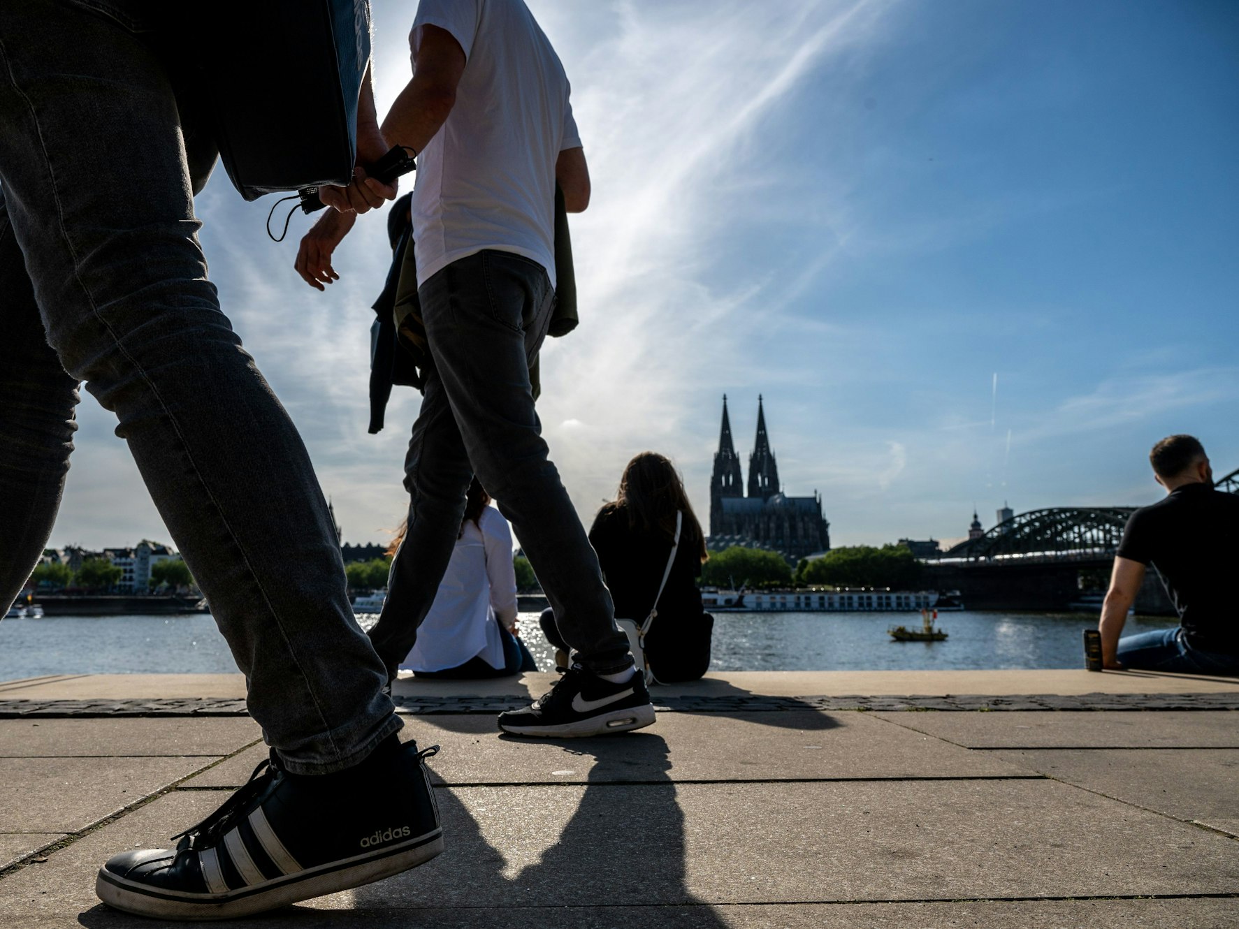 Am Rheinboulevard flanieren junge Leute durch den Sonnenschein.