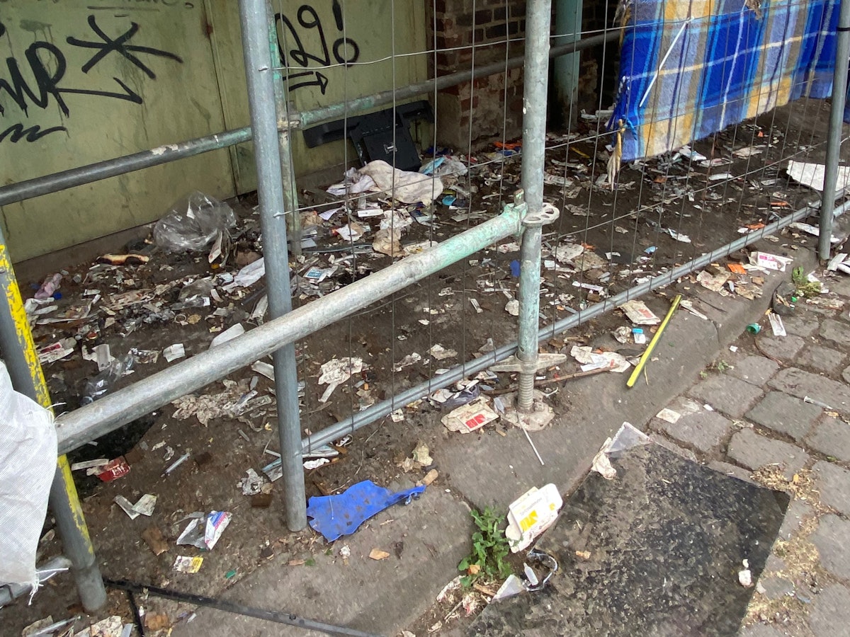 Unterhalb eines Gerüsts liegen unzählige benutzte Spritzen, Spritzenverpackungen, Kondome und weiterer Müll.