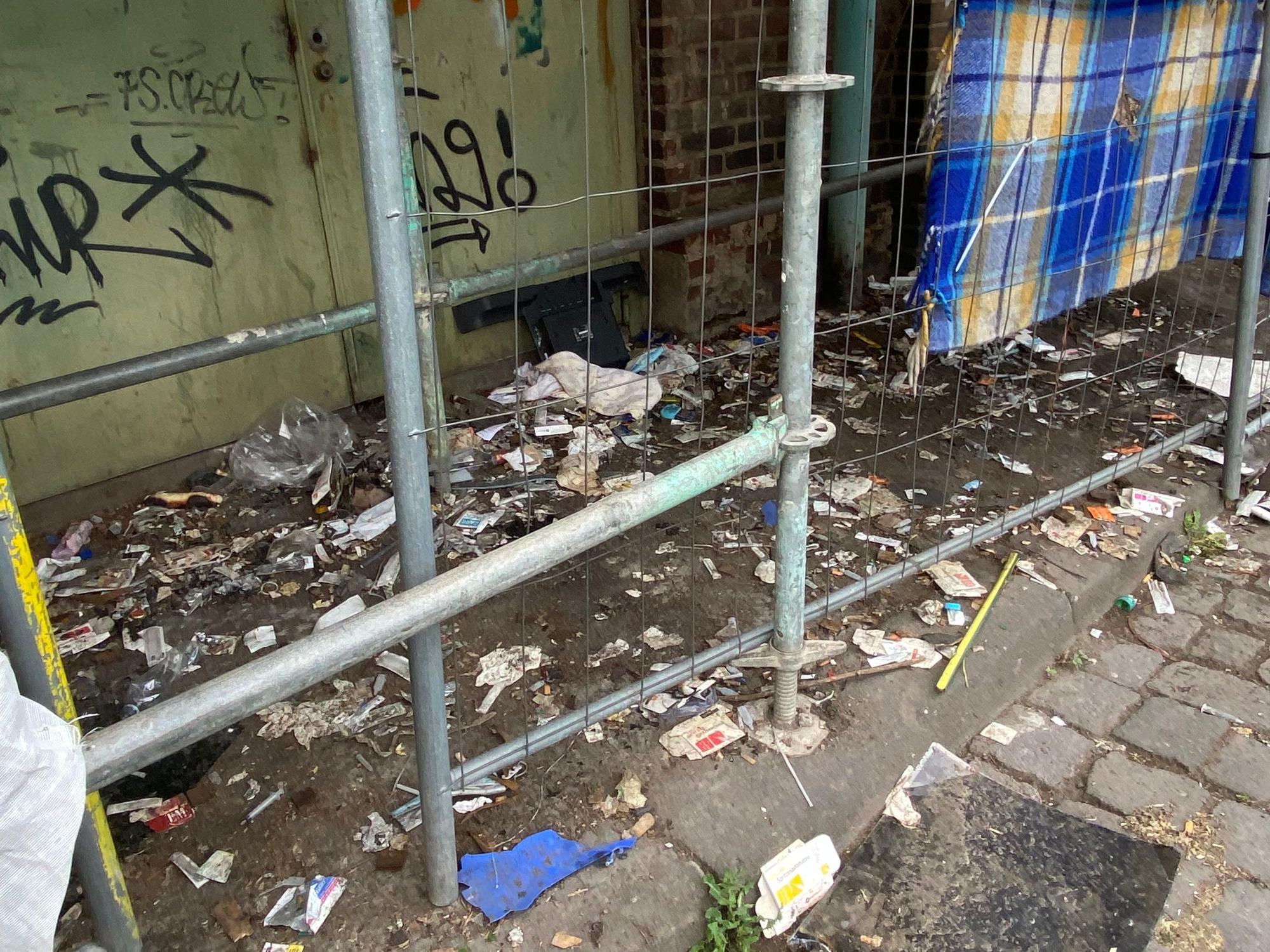 Unterhalb eines Gerüsts liegen unzählige benutzte Spritzen, Spritzenverpackungen, Kondome und weiterer Müll.