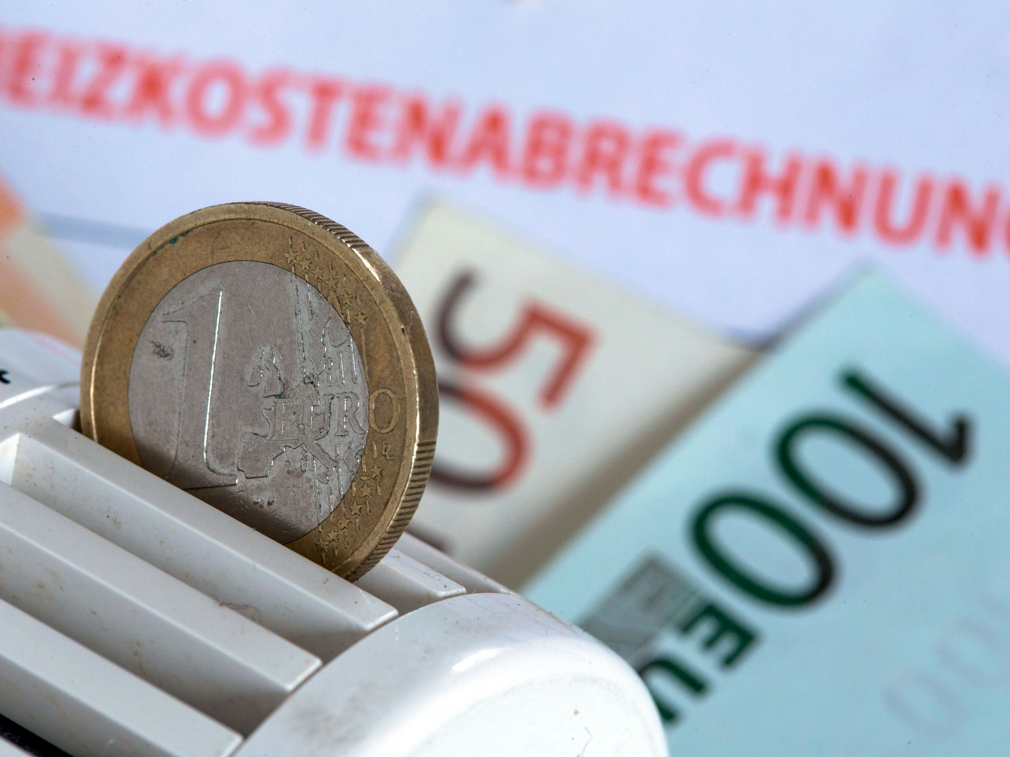 Eine Euromünze steckt am 04. Dezember 2014 in einem Heizungsthermostat, der auf einer Heizkostenabrechnung und Euro-Geldscheinen liegt.