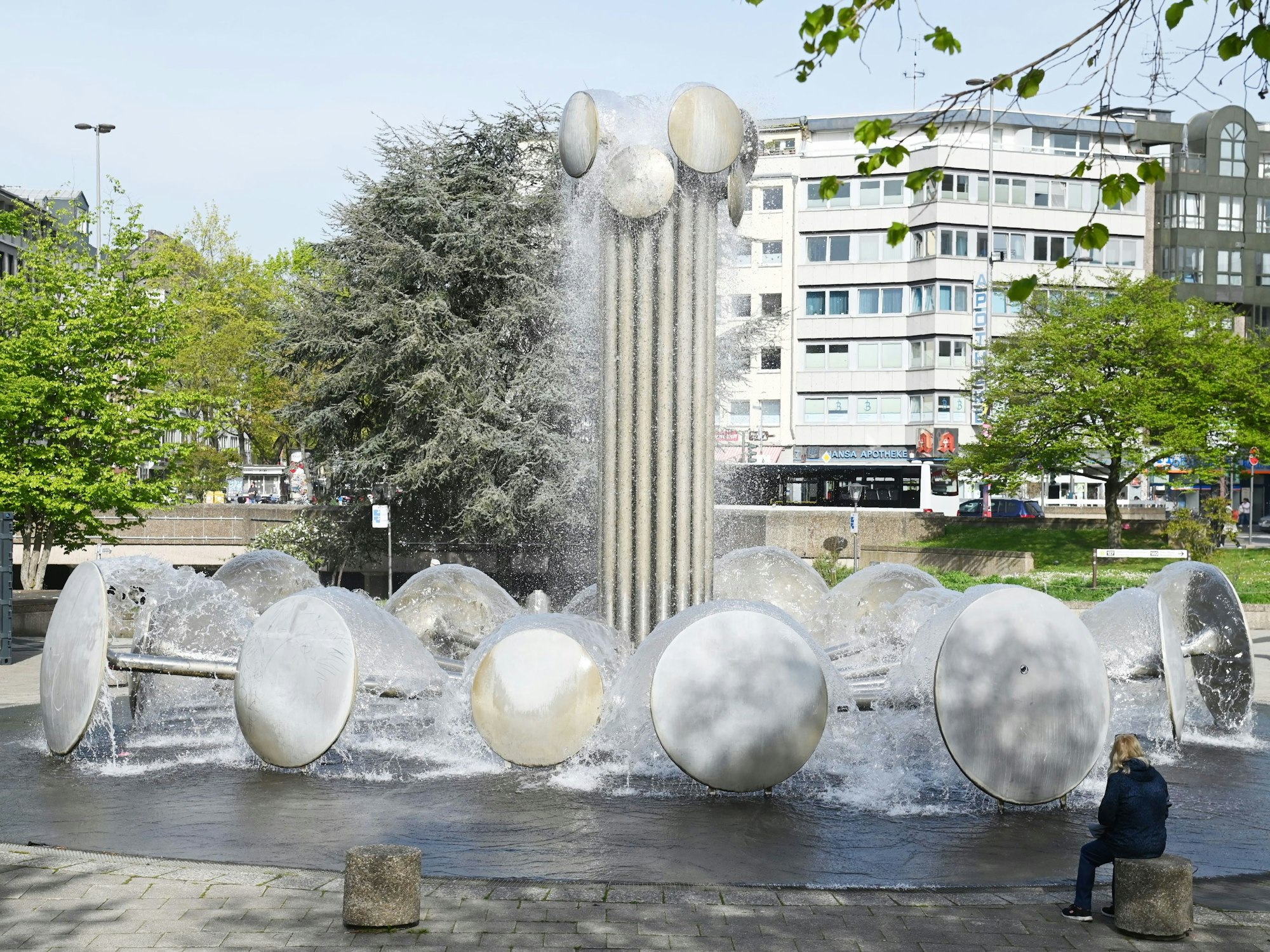 Der Ebertplatz in Köln mit prominentem Brunnen und Bäumen im Hintergrund.