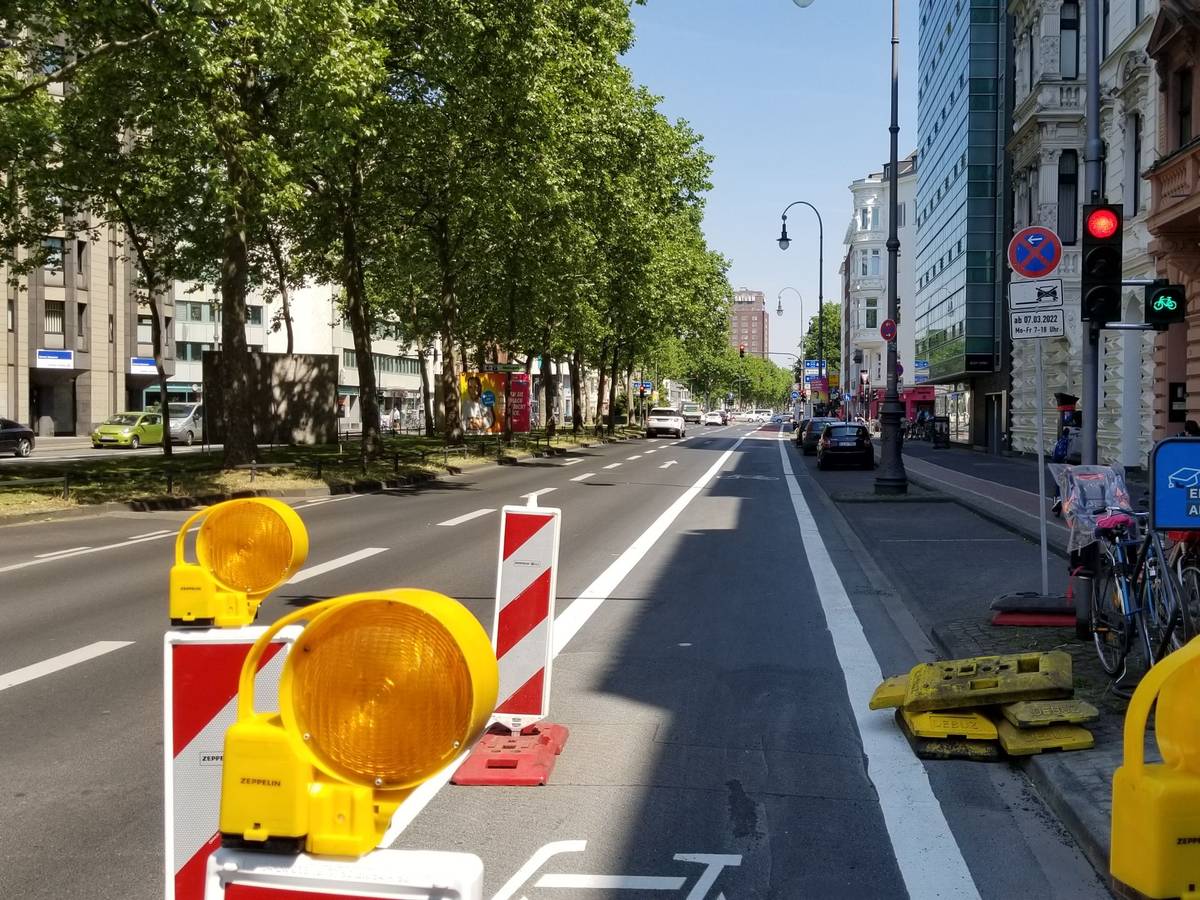 Der Hansaring in Höhe der Ausfahrt des Parkhauses auf den Kaiser-Wilhelm-Ring. Rechts steht eine Ampel, die für Autofahrer und Autofahrerinnen rot zeigt. Fahrradfahrer und Fahrradfahrerinnen müssen hier nicht halten, die Ampel ist grün.