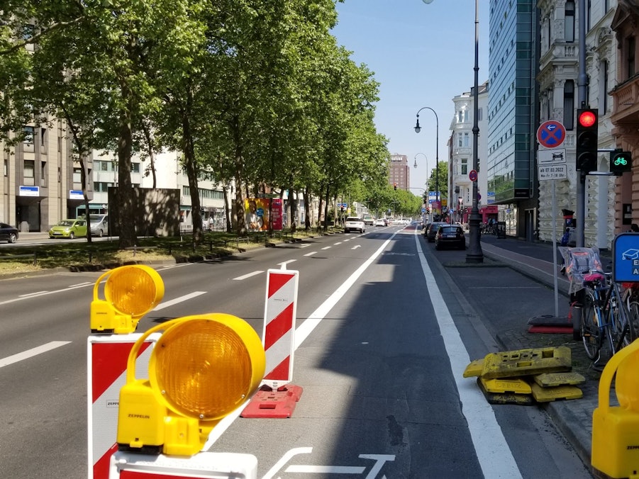 Der Hansaring in Höhe der Ausfahrt des Parkhauses auf den Kaiser-Wilhelm-Ring. Rechts steht eine Ampel, die für Autofahrer und Autofahrerinnen rot zeigt. Fahrradfahrer und Fahrradfahrerinnen müssen hier nicht halten, die Ampel ist grün.