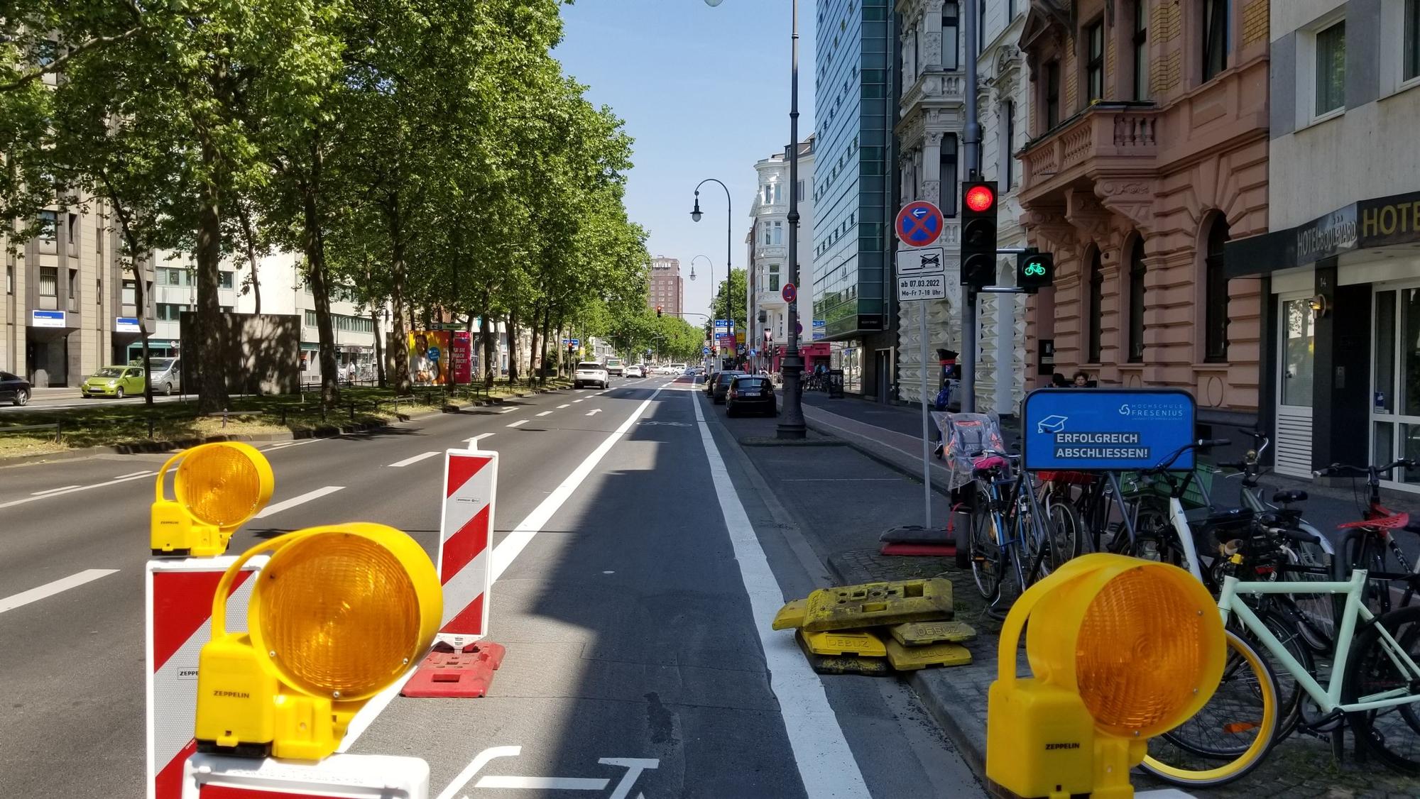 Der Hansaring in Höhe der Ausfahrt des Parkhauses auf den Kaiser-Wilhelm-Ring. Rechts steht eine Ampel, die für Autofahrer und Autofahrerinnen rot zeigt. Fahrradfahrer und Fahrradfahrerinnen müssen hier nicht halten, die Ampel ist grün.