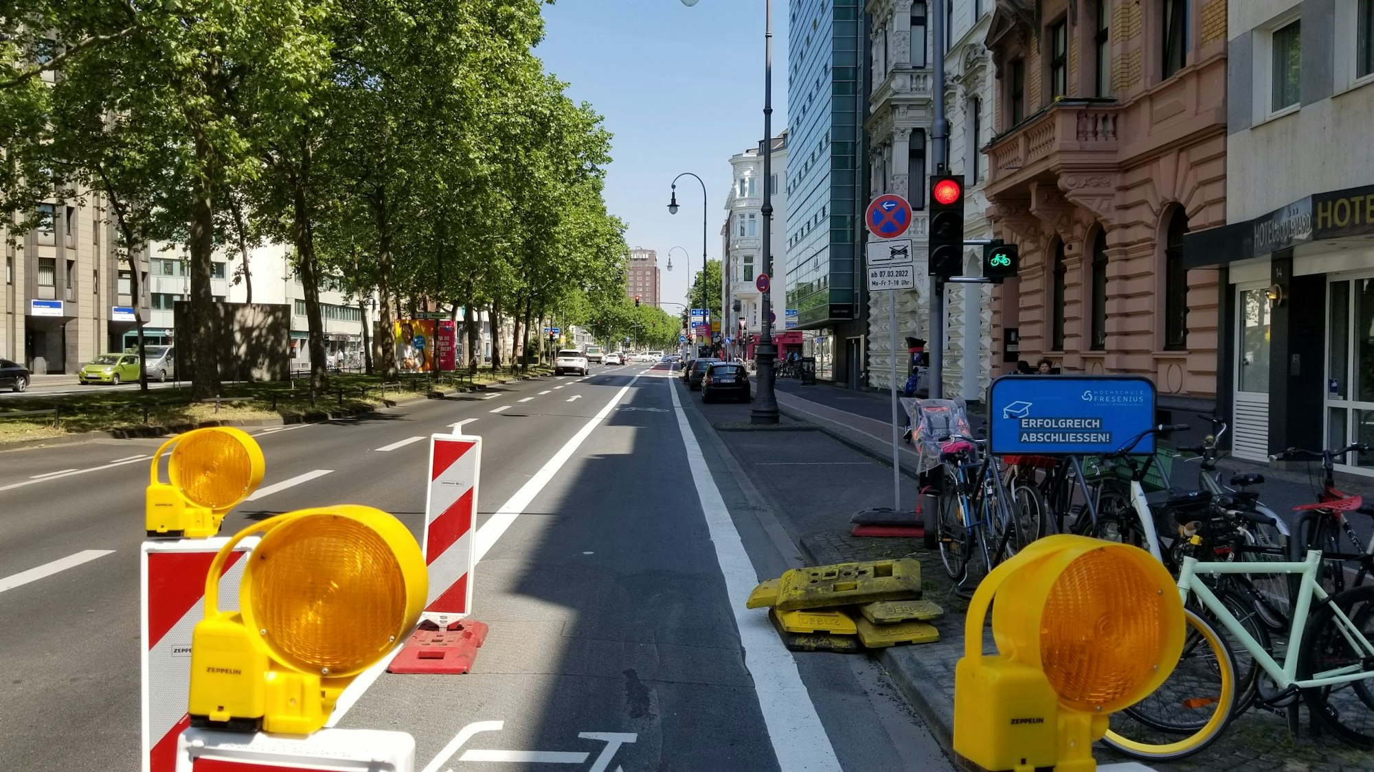 Der Hansaring in Höhe der Ausfahrt des Parkhauses auf den Kaiser-Wilhelm-Ring. Rechts steht eine Ampel, die für Autofahrer und Autofahrerinnen rot zeigt. Fahrradfahrer und Fahrradfahrerinnen müssen hier nicht halten, die Ampel ist grün.