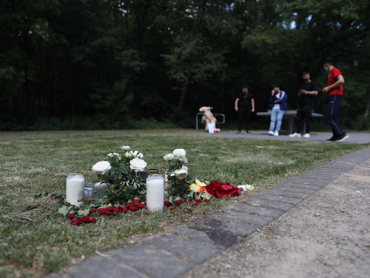 Auf einem Spielplatz liegen Blumen und stehen Kerzen. Im Hintergrund befinden sich mehrere Jugendliche an einer Tischtennisplatte.