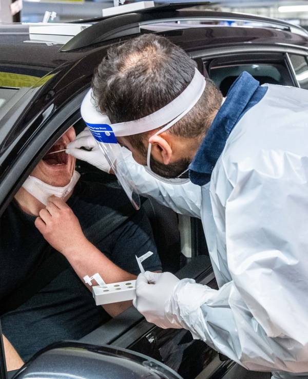 Ein Mitarbeiter eines Drive-In Testzentrums in Köln führt bei einem Autofahrer durch das geöffnete Fenster einen Schnelltest im Rachen durch.