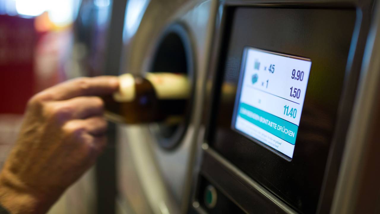 Eine Person legt eine Glasflasche in einen Pfandautomaten.