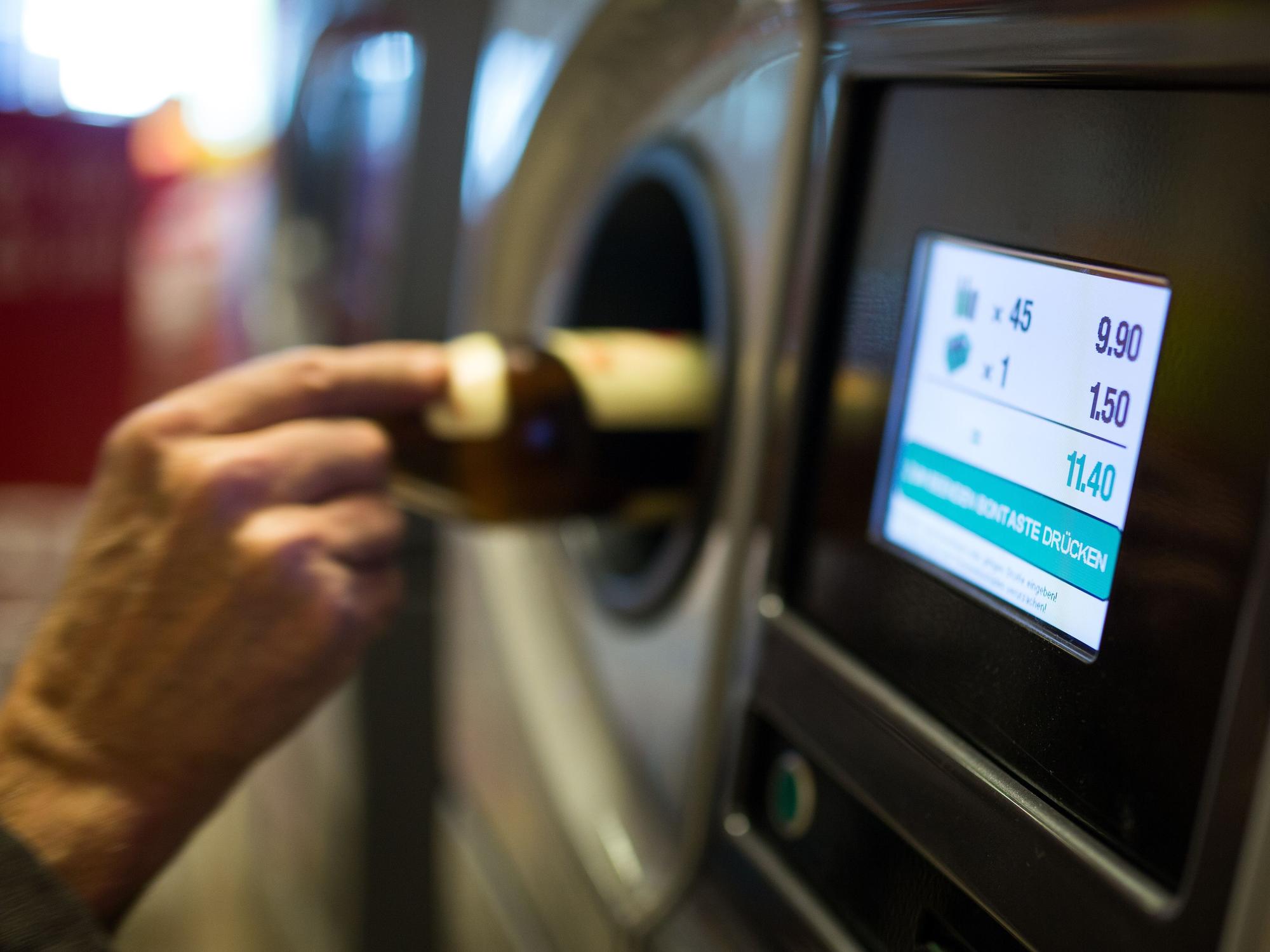Eine Person legt eine Glasflasche in einen Pfandautomaten.