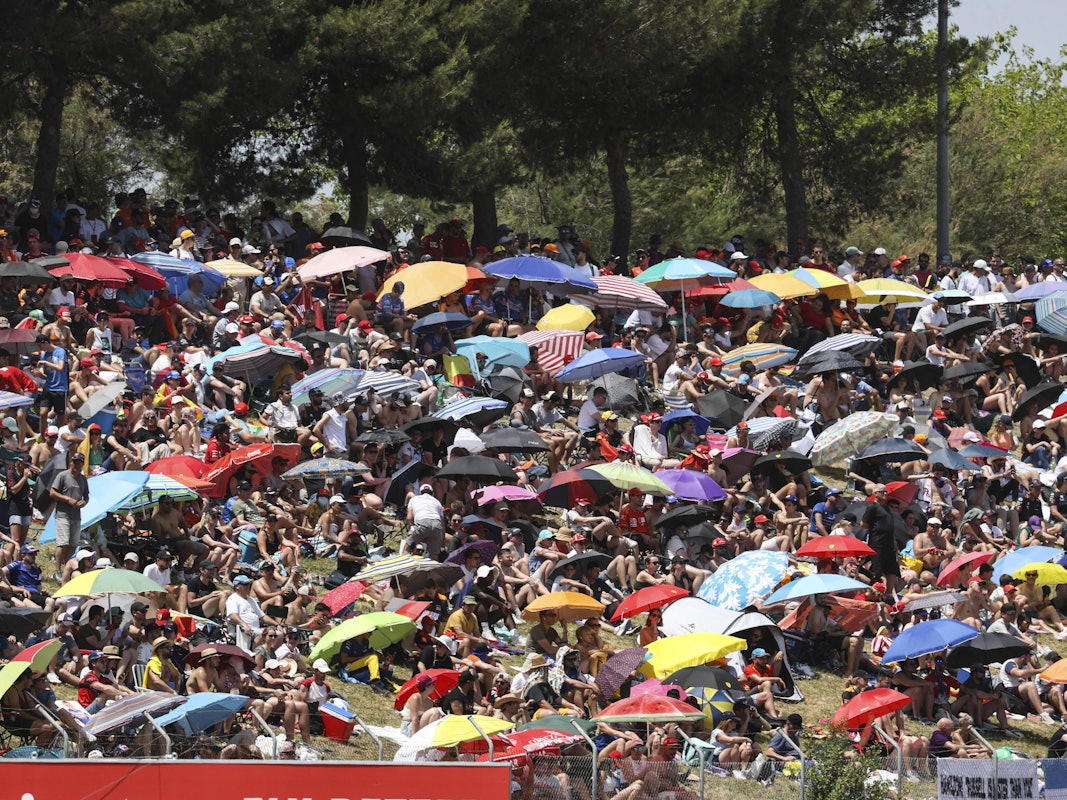 Auf den Zuschauerrängen schützen sich unzählige Zuschauer mit Sonnenschirmen vor der Hitze.