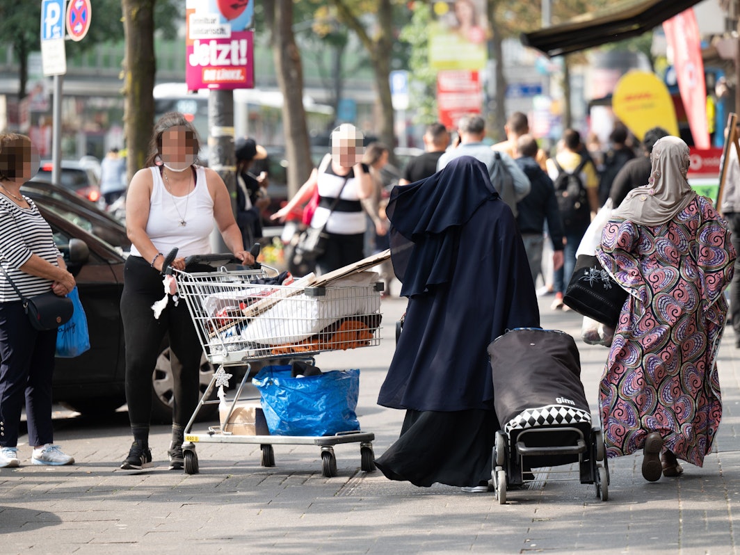 Eine Frau steht mit einem Einkaufswagen auf einem Gehweg in Köln.