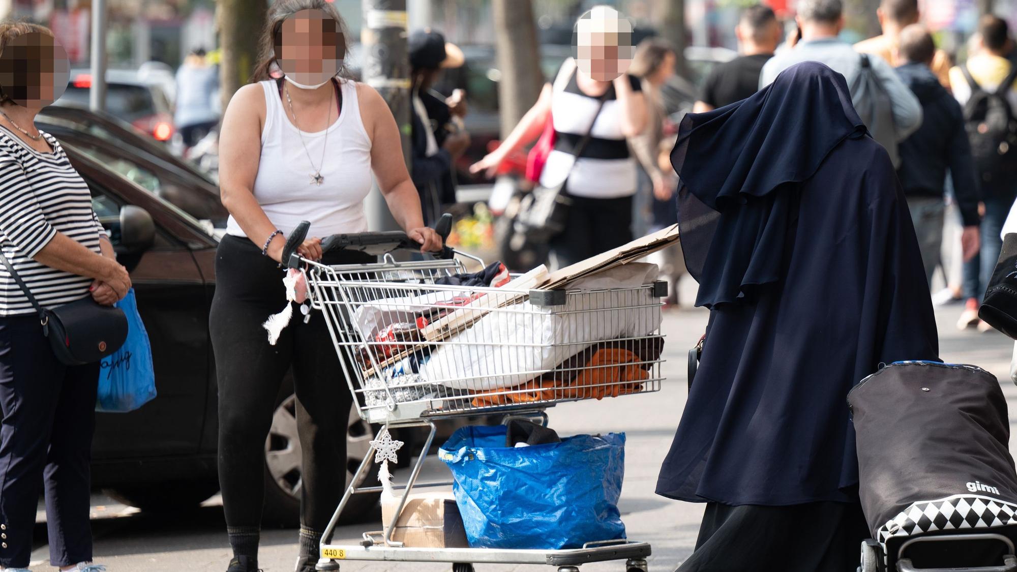 Eine Frau steht mit einem Einkaufswagen auf einem Gehweg in Köln.