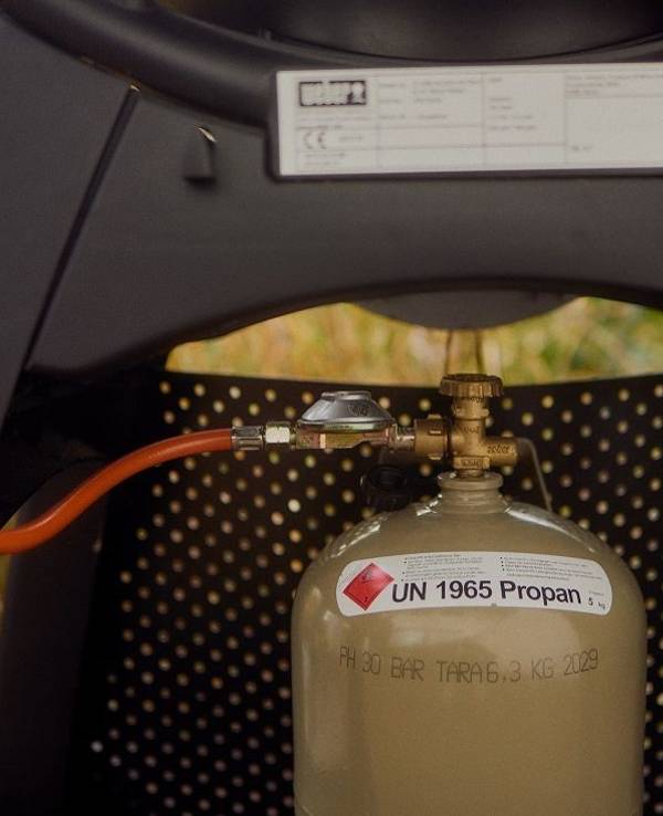 Eine Flasche Gas ist an einen Gasgrill angeschlossen.