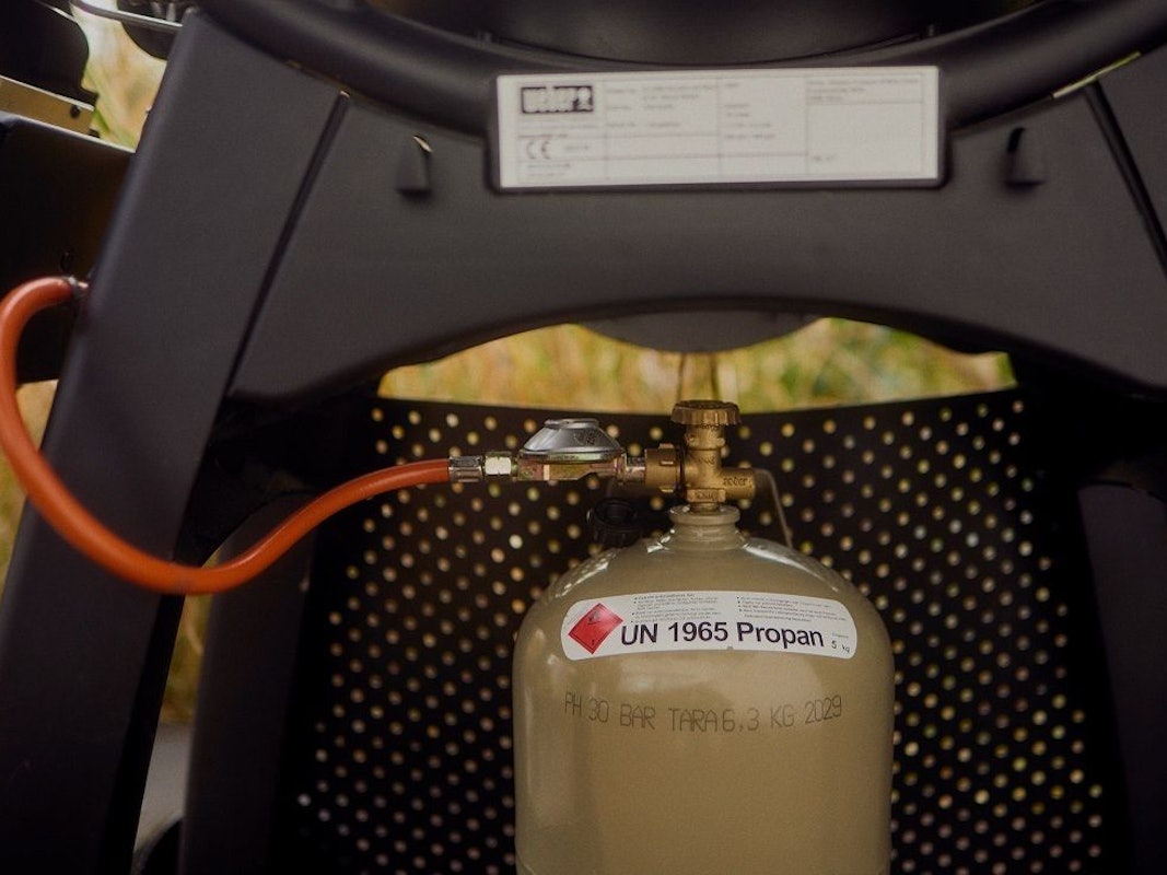 Eine Flasche Gas ist an einen Gasgrill angeschlossen.